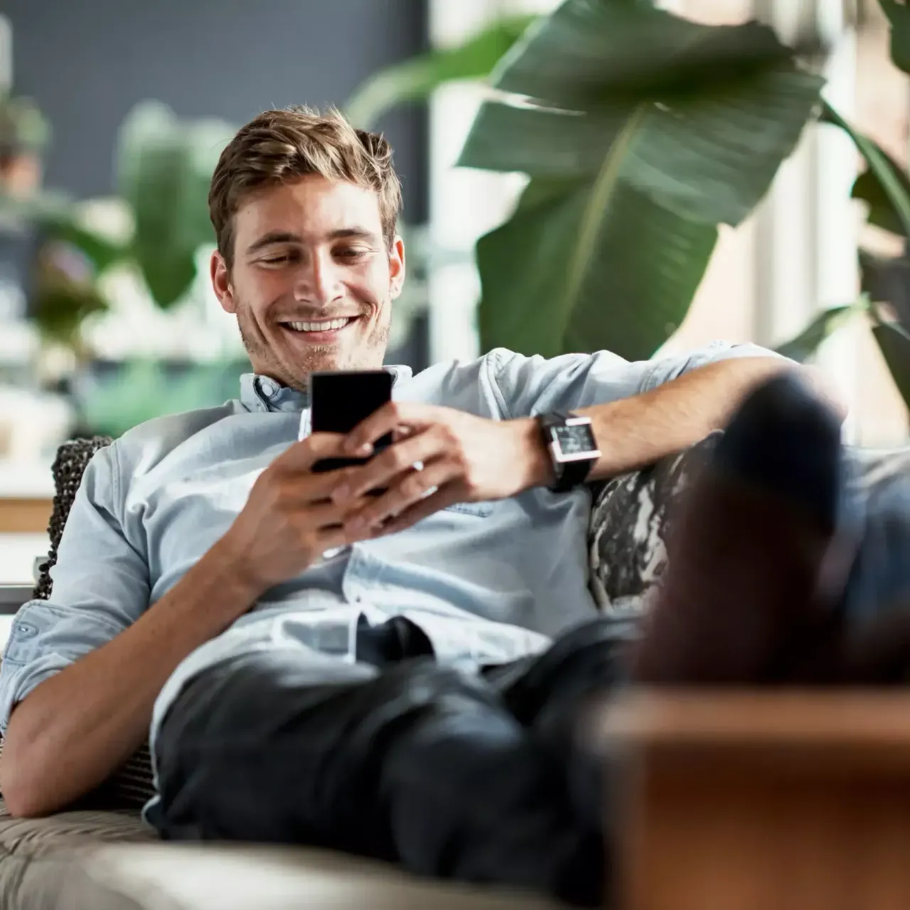 Ein Mann liegt mit seinem Handy auf der Couch und lacht.