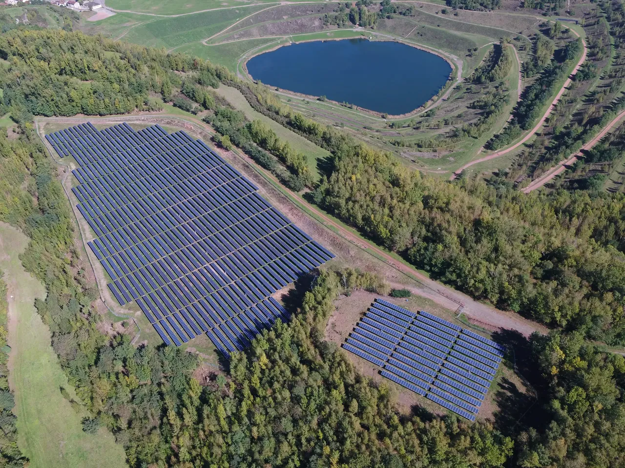 Es wird aus der Vogelperspektive der klimavest Solarpark Decazville in Frankreich mit daneben liegendem See dargestellt.