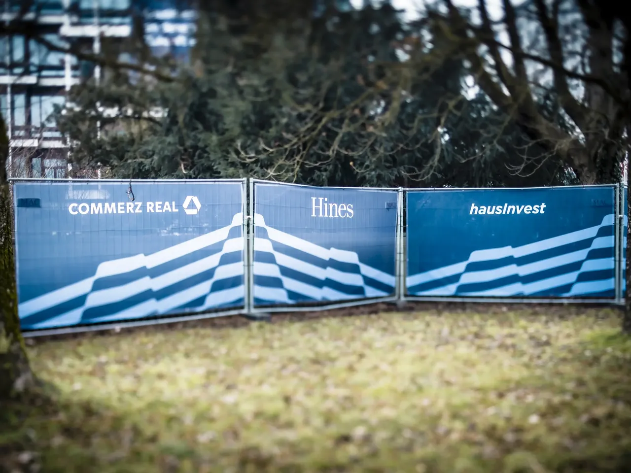 Im Rahmen der Eröffnung der KI-Fabrik am Tucherpark im Eisbachviertel werden 3 Werbebanner auf einem Bauzaun der Projektbeteiligten Commerz Real, Hines und hausInvest dargestellt.