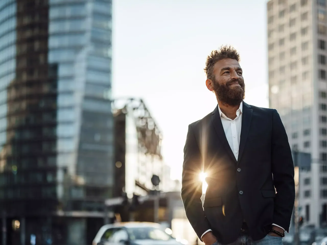 Ein Mann Ende 30 im schwarzen Jacket steht in Berlin am Potsdamer Platz in seinem Jacket spiegelt sich die untergehenede Sonne