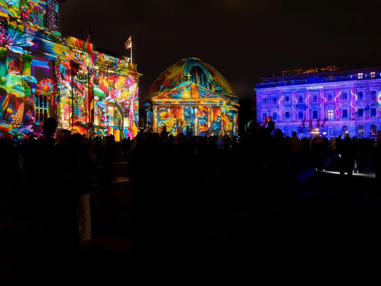 Es wird das Festival of Lights 2025 mit dem illuminierten Bebelsplatz und dem ehemaligen hausInvest Gebäude Hotel de Rome dargestellt.