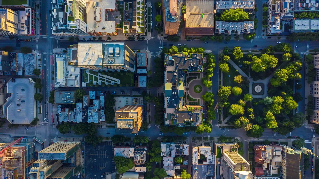 Es wird aus der Vogelperspektive ein Stadtviertel mit dem Blick auf die Dächer von Hochhäusern und eine Grünanlage dargestellt.