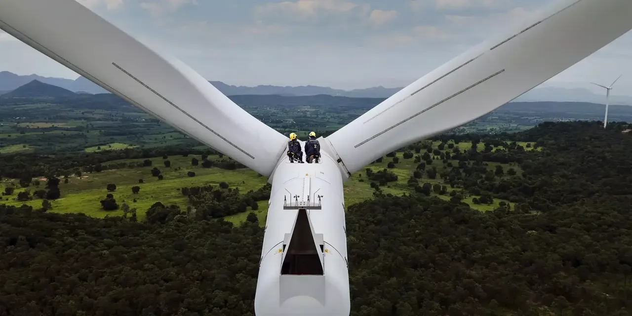 klimaVest: Zwei Arbeiter sitzen auf einem Windrad. Sie tragen gelbe Helme und Klettergurte. Sie sitzen in der Wartungsluke.