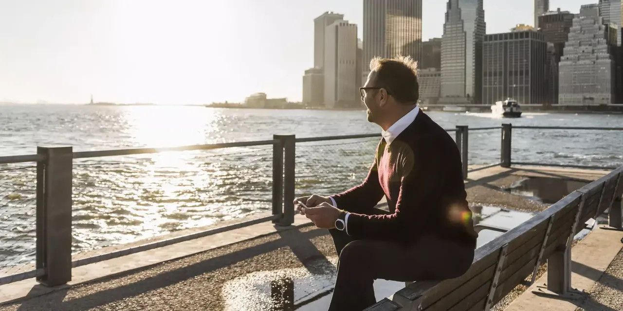 Ein Mann Mitte 50 sitzt am Ufer des Hudson Rivers in New York City und schaut auf das Wasser