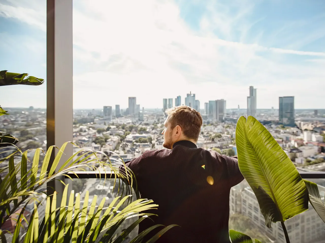 Außenansicht: Designer Sebastian Herkner steht auf einem Balkon der hausInvest Immobilie One Forty West in Frankfurt am Main und schaut auf die Frankfutert Skyline