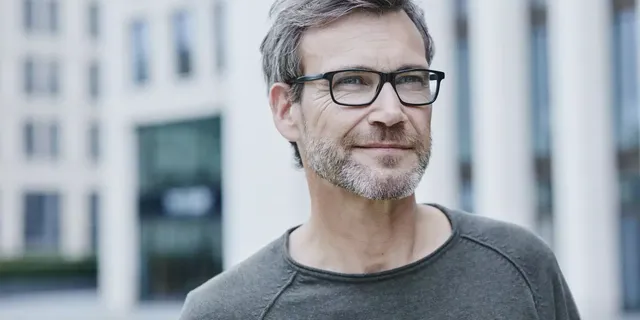 Ein Mann Mitte 40 mit einer schwarzen Brille, der vor einer Immobilie steht