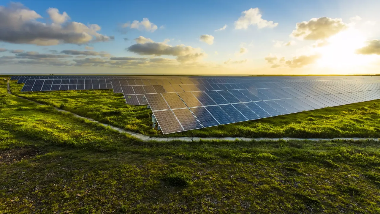 Es wird eine Solarkraftanlage im auf einer grünen Wiese dargestellt, im Hintergrund einen Sonnenaufgang.