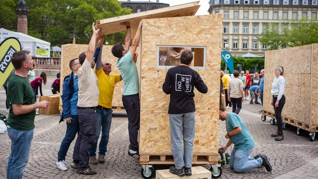 Commerz Real Mitarbeiter bauen in Teamarbeit Little Home Obdachlosen-Unterkünfte