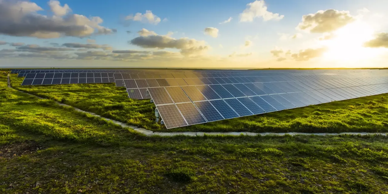 Es wird eine Solarkraftanlage im auf einer grünen Wiese dargestellt, im Hintergrund einen Sonnenaufgang.