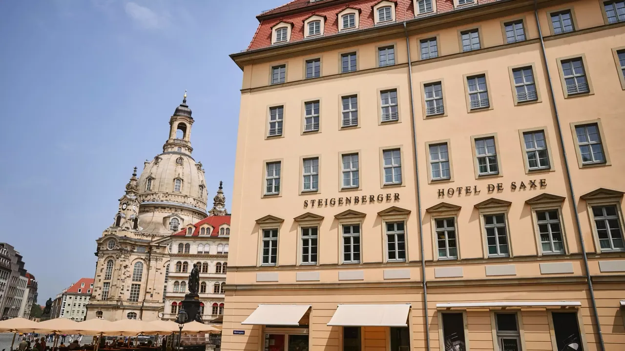 Es wird die Außenansicht der hausInvest Immobilie Hotel de Saxe in Dresden dargestellt, im Hintergrund ist die Frauenkirche zu sehen.