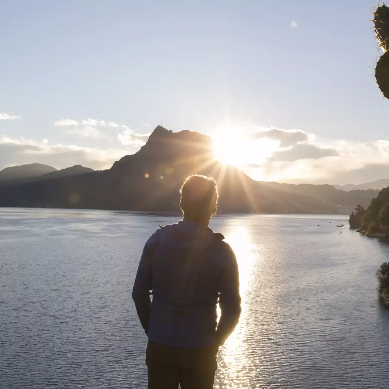 klimaVest: Mann steht mit Händen in den Hosentaschen am Ufer des Meeres und guckt sich den Sonnenuntergang an.