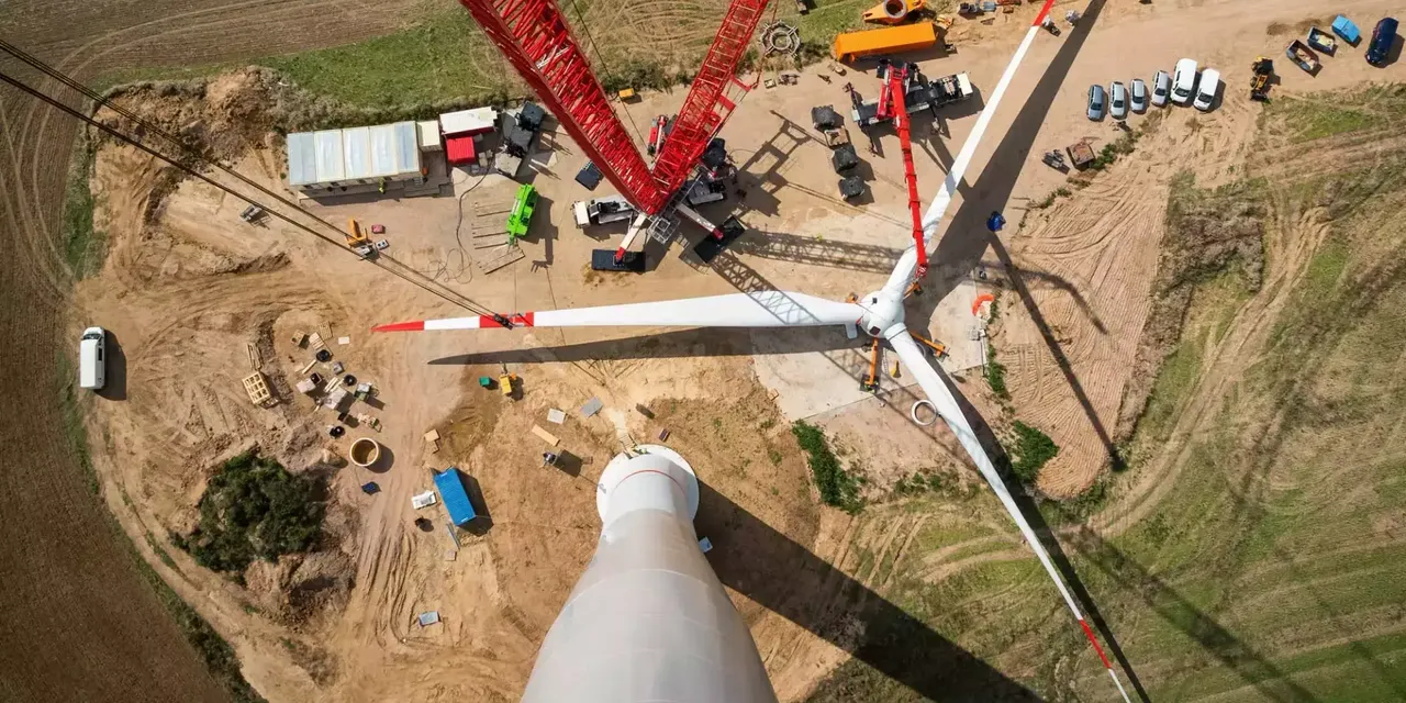 klimaVest:
  Luftaufnahme des Aufbaus eines Windrades mit Fahrzeugen und einem Kran.