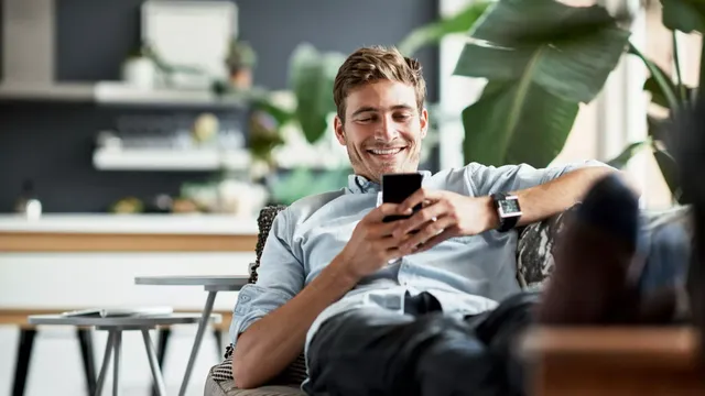 Ein Mann liegt mit seinem Handy auf der Couch und lacht.