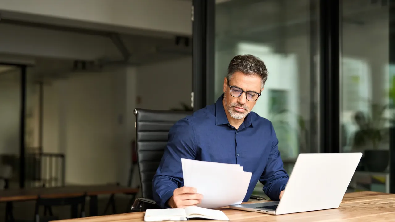 Mittelalter Mann vor Papieren und Laptop am Schreibtisch