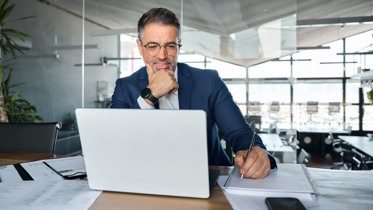 Mann mit Brille und in Anzug sitzend vor einem Laptop