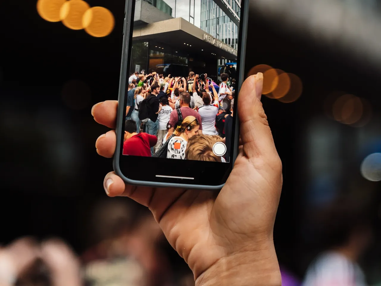 Eine Person nutzt ihr Handy, um die Menschenmasse vor der hausInvest-Immobilie One Forty West zu fotografieren.