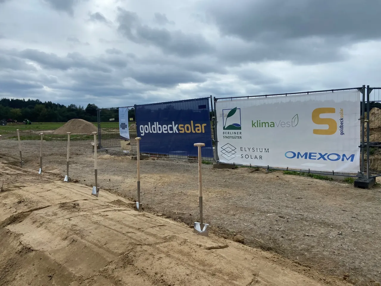 Es wird im Rahmen des Spatenstichs der Bauzaun mit den entsprechenden Logos des Projektbeteiligten des Agri-PV-Projekts in Berlin-Schönefeld dargestellt.