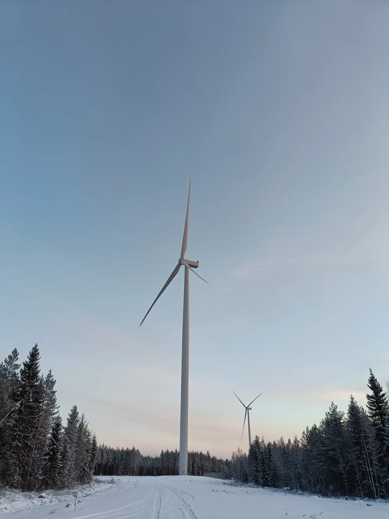 In einer Schneelandschaft wird die Außenansicht von zwei Windrädern des klimaVest Windparks Fennica in Finnland abgebildet.